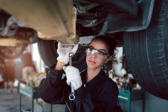 Beautiful female auto mechanic checking wheel tires in garage, car service technician woman repairing customer car at automobile service, inspecting vehicle underbody and suspension engine system.
