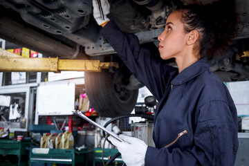 Beautiful female auto mechanic checking wheel tires in garage, car service technician woman repairing customer car at automobile service, inspecting vehicle underbody and suspension engine system.