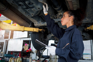 Beautiful female auto mechanic checking wheel tires in garage, car service technician woman...