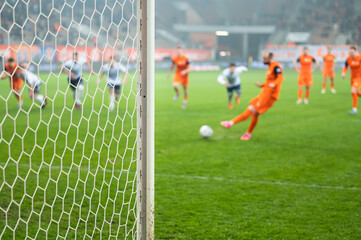 Detail of goal's post with net and football player during penalty kick in the background.
