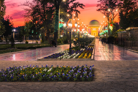 Park Kamal Khudzhandi central alee with beautiful evening illumnation, sunset glow and Kamoli Khujand mausoleum in background . Khujand, Tajikistan.