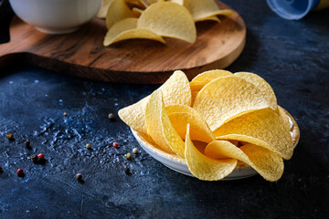 Close-up of beautiful potato chips and sauce in a white bowl on a wooden cutting board. On a dark abstract background.