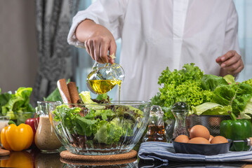 woman chef mix fresh baby cos salad and pour salad dressing in glass blow. Organic Vegetables mix all green salad In glass bowl. Breakfast fresh salad and clean vegetable.