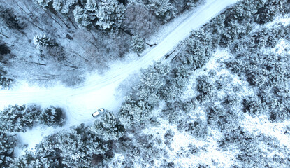 white car is moving at high speed on a snowy forest road. Drone photo.