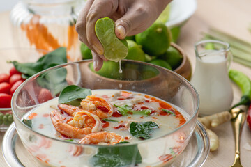 Tom Yam Kung or Tom Yum soup is Thai hot spicy soup shrimp or prawn with lemon grass, lemon, galangal, mushrooms, coconut milk and chili in bowl on wooden table top view, famous Thai food cuisine.