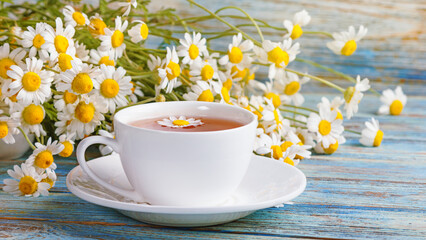 Daisy flowers in a white cup of tea, chamomile herbs on wooden background. Herbal medicine. Healthy lifestyle concept.