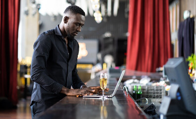 handsome young African American man looking at laptop computer screen. Black businessman working on laptop computer at the club.