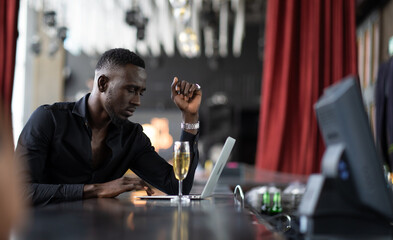 handsome young African American man looking at laptop computer screen. Black businessman working on laptop computer at the club.