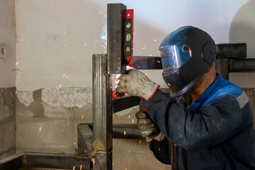 An experienced man   using a spirit level and welding a seam on a spiral staircase at a...
