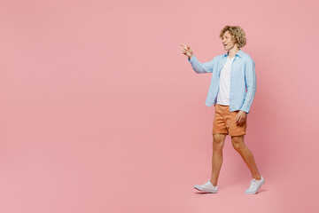Fototapeta na wymiar Full body side view young cool happy caucasian blond man wear blue shirt white t-shirt waving hand walk go strolling isolated on plain pastel light pink background studio portrait. Lifestyle concept.