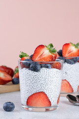Chia pudding with strawberries and blueberries, chia seeds on a pink background. Healthy breakfast concept. Copy space. 