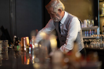 Professional expert barman making mix cocktail on counter bar at night club. Senior man