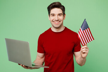 Young smiling fun happy smart IT man he wearing red t-shirt casual clothes hold American flag use...