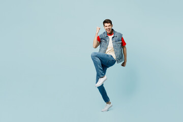 Full body young man he wears denim vest red t-shirt casual clothes doing winner gesture celebrate clenching fists say yes isolated on plain pastel light blue cyan background studio. Lifestyle concept.