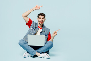 Full body young happy IT man he wears denim vest red t-shirt casual clothes hold use work on laptop...