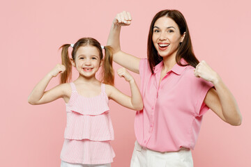 Happy woman wear casual clothes with child kid girl 6-7 years old. Mother daughter show biceps muscles on hand demonstrating strength isolated on plain pastel pink background Family parent day concept