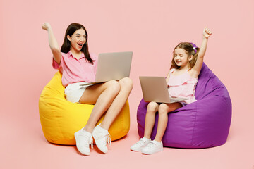 Full body IT woman wear casual clothes with child kid girl 6-7 years old. Mother daughter sit in bag chair work hold use laptop pc computer isolated on plain pink background Family parent day concept.