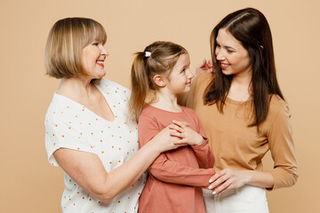 Happy positive women wearing casual clothes with child kid girl 6-7 years old. Granny mother daughter hug cuddling looking to each other isolated on plain beige background. Family parent day concept.