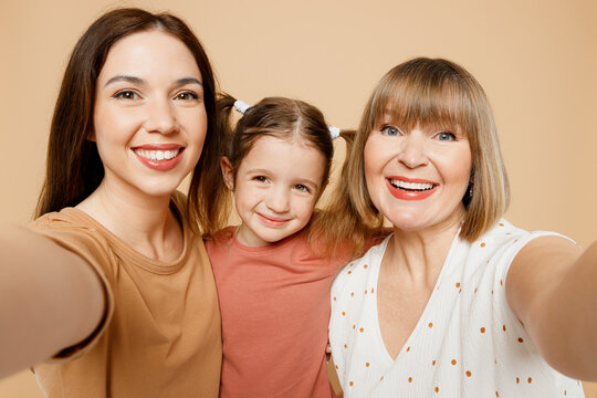 Close up happy women wear casual clothes with child kid girl 6-7 years old. Granny mother daughter do selfie shot pov on mobile cell phone isolated on plain beige background. Family parent day concept