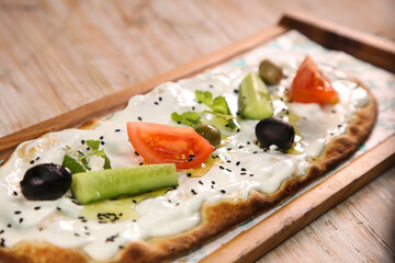 Labneh pizza bread with olives, tomato and cucumber served in wooden board isolated on background...