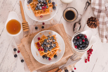 Waffles with red currant and blueberries on white dish.