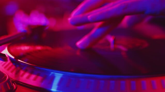 DJ carefully doing scratches using a record rotating at the turntable during the studio recording of the vinyl session in a color light close up