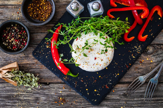 Cheese Robiola d'Alba with chili and thyme on black stone board on wooden table