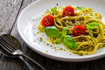 Noodles with basil pesto, parmesan cheese, tomatoes and basil leaves served on wooden table 