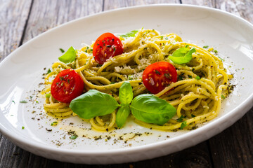 Noodles with basil pesto, parmesan cheese, tomatoes and basil leaves served on wooden table 