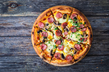 Circle pizza with sausages, onion and mozzarella cheese on wooden table 