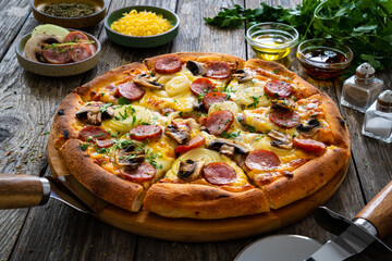 Circle pizza with sausages, onion and mozzarella cheese on wooden table 