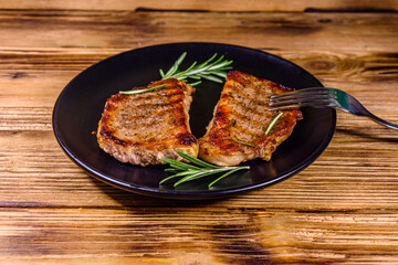 Plate with roasted steaks and rosemary twigs on a wooden table
