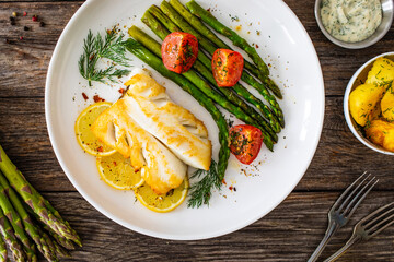 Fried halibut loin with cooked green asparagus and tomatoes on wooden table
