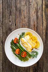 Fried halibut loin with cooked green asparagus and tomatoes on wooden table
