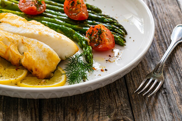 Fried halibut loin with cooked green asparagus and tomatoes on wooden table
