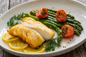 Fried halibut loin with cooked green asparagus and tomatoes on wooden table
