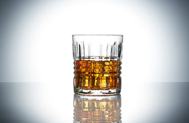 Crystal glass of whiskey with ice cubes on grey gradient background. Glass of scotch whiskey and ice on grey gradient background. Glass of whiskey on a glossy surface