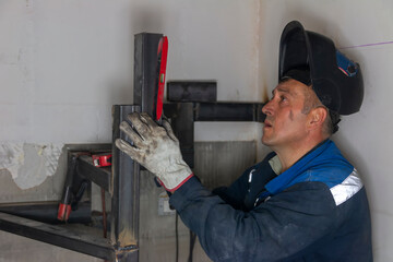 An experienced man   using a spirit level and welding a seam on a spiral staircase at a...