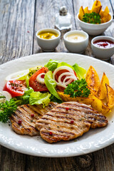 Barbecued pork chops with fried potatoes and fresh vegetables on wooden table
