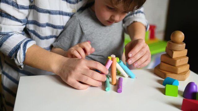 Woman and little boy play with plastiline and build tower. Kids hands with colorful clay closeup.  Early childhood development and behavior modification. Speech therapist work and help