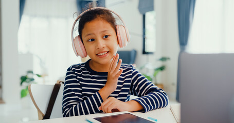Asian toddler girl with sweater wear headphone sit front of desk with notepad use magic pen focus on writing do homework, finger counting number math online learning course from laptop at home. - obrazy, fototapety, plakaty