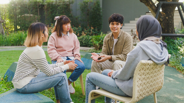 Small Asian group of people sit in a close circle and talk to a therapist in park. Smile people sharing story happy speak diverse people sitting in circle at group therapy session with psychologist.