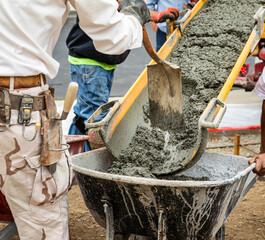 Wet cement off loaded by construction workers from a cement truck chute into a wheelbarrow