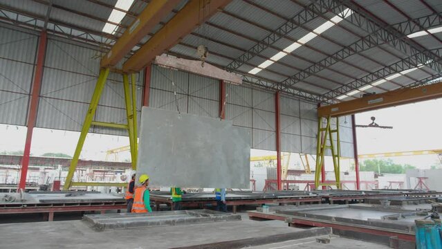 Team young asian engineer man walking while crane lifting precast concrete wall panel with professional at industrial factory, worker working with construction site, industry and transport concept.
