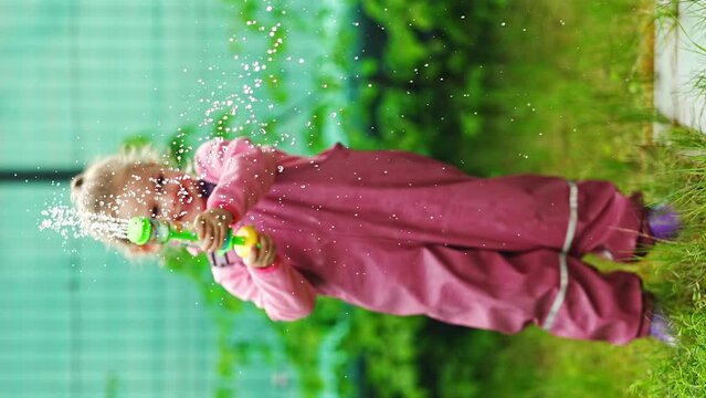 Happy laughing child girl 2-3 year old wearing waterproof clothes have a fun with water gun on home backyard Generative AI