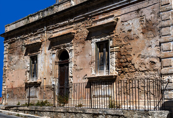 Fototapeta na wymiar old abandoned and decaying one-storey house with a door and two windows, built in the typical Sicilian style, against an intensely blue sky