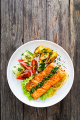 Seared salmon steak with fried potatoes and fresh vegetable salad served on wooden table
