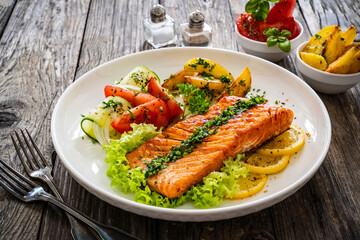 Seared salmon steak with fried potatoes and fresh vegetable salad served on wooden table
