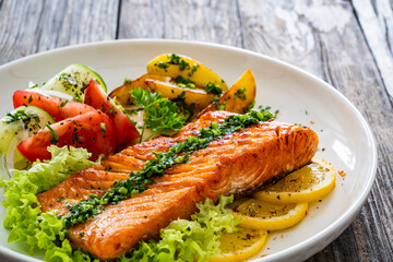 Seared salmon steak with fried potatoes and fresh vegetable salad served on wooden table

