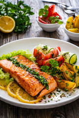 Seared salmon steak with fried potatoes and fresh vegetable salad served on wooden table
